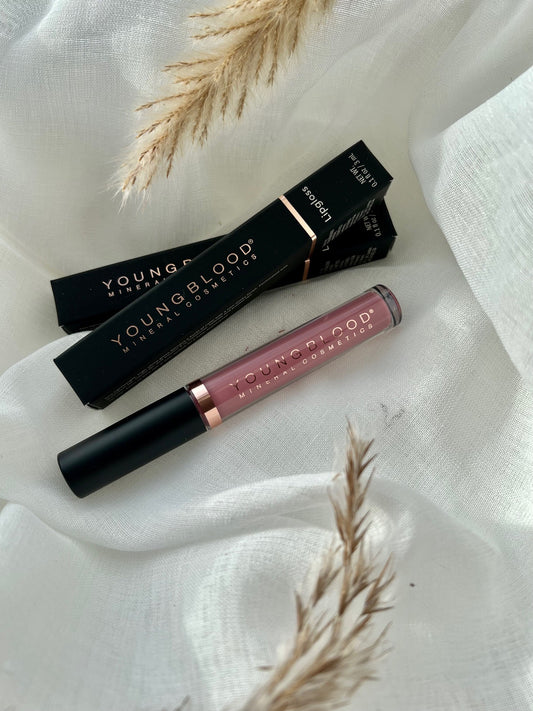 Young Blood Lipgloss i farven Amour. Luksuriøs lipgloss med skinnende finish, der giver læberne et fyldigt og blødt udseende. Den romantiske Amour-nuance fremhæver læbernes naturlige skønhed med et elegant skær. Produktet vises i Young Bloods karakteristiske elegante emballage.